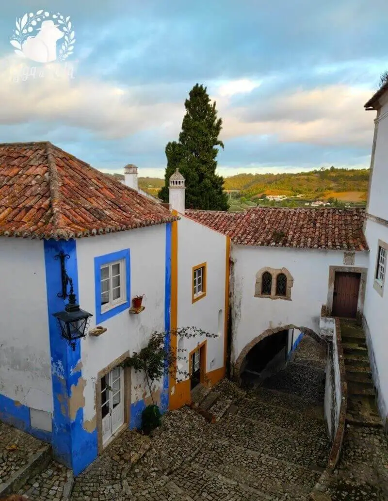 Vista panorâmica da Vila de Óbidos, capturando as casas brancas e as muralhas históricas ao fundo, cercadas pela paisagem verdejante.
