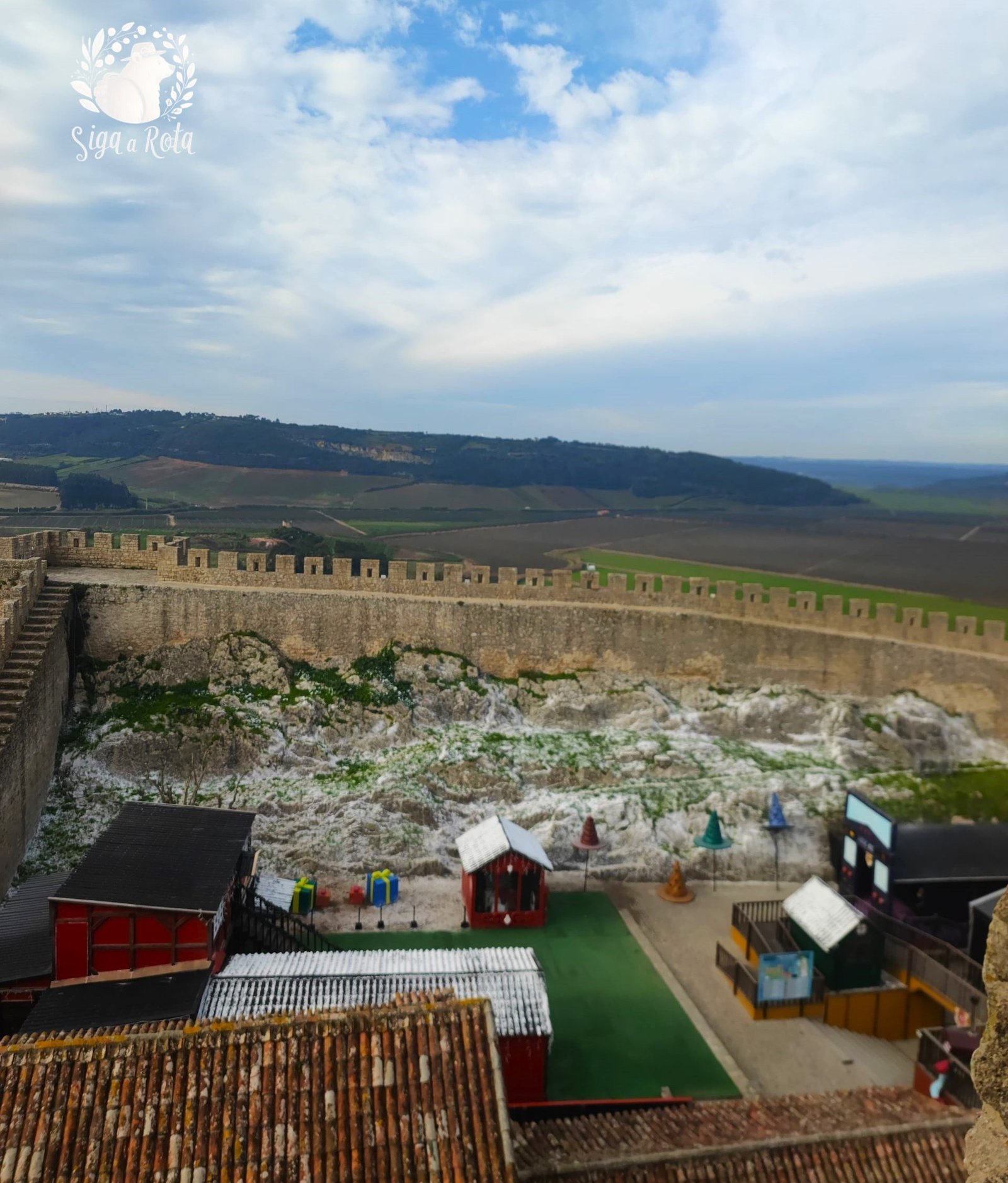 Vista panorâmica das muralhas da Vila de Óbidos decoradas com luzes de Natal, proporcionando uma paisagem encantadora.