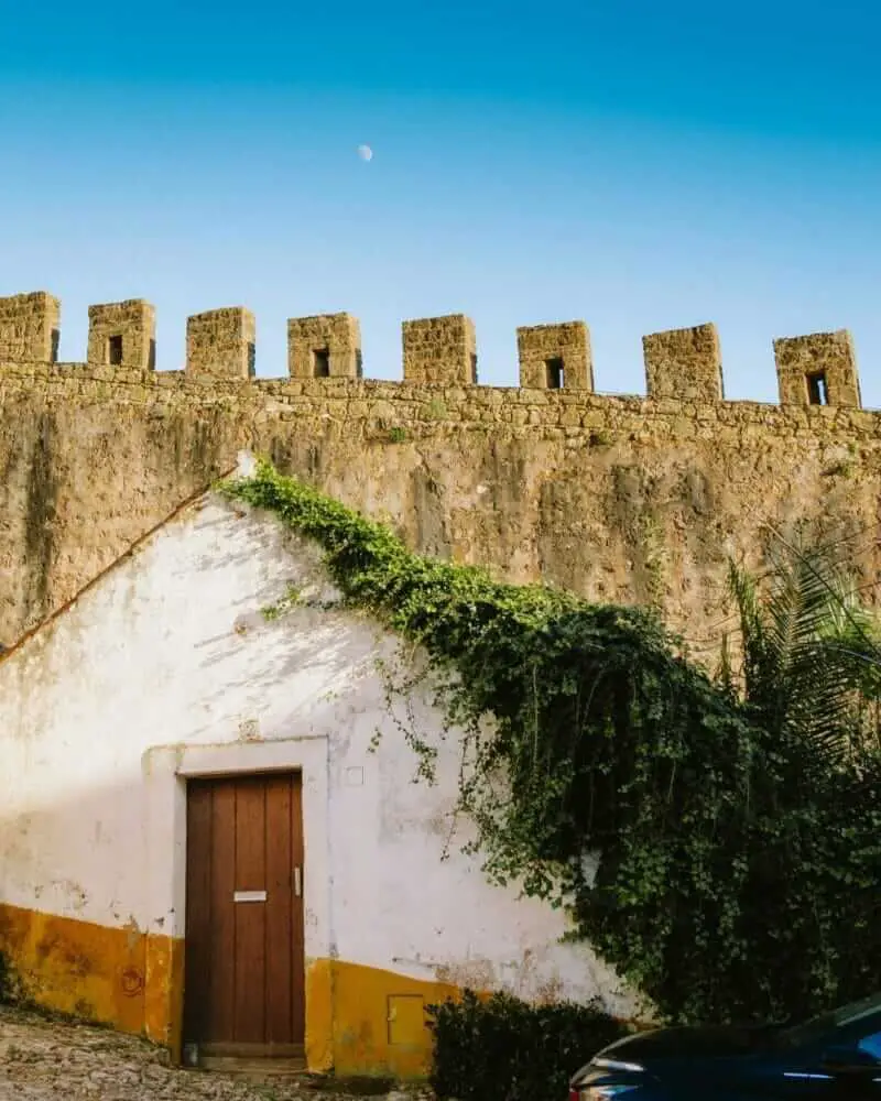 Aldeia de Óbidos com castelo e ruas de paralelepípedos cercadas de flores, Portugal