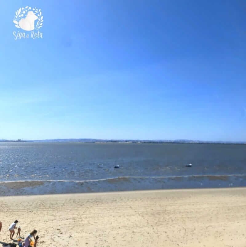 Vista ampla da Praia Fluvial do Rosário, com areia e o rio Tejo ao fundo.