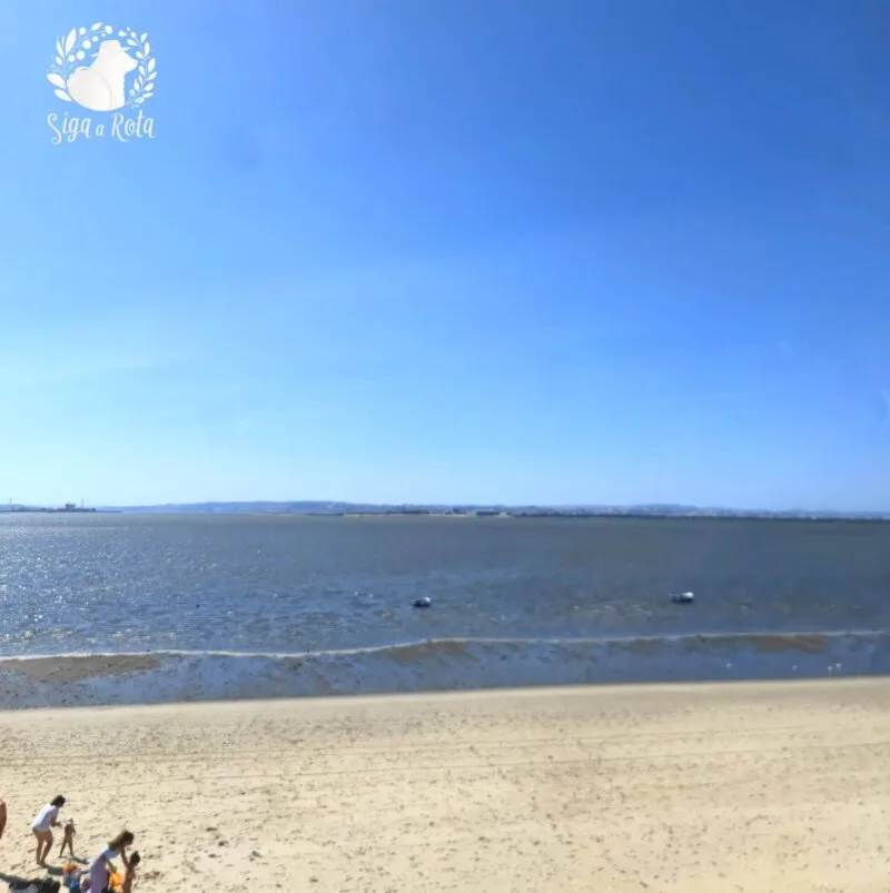 Vista ampla da Praia Fluvial do Rosário, com areia e o rio Tejo ao fundo.