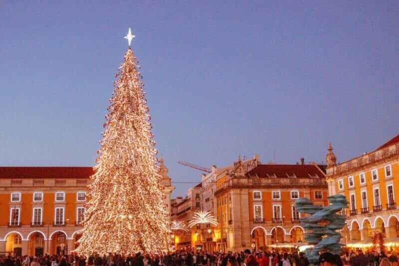 Árvore de Natal iluminada na Praça do Comércio, Lisboa, com luzes e decorações festivas.
