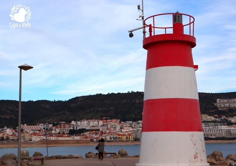 Farol de Sesimbra com barcos ancorados ao redor e o horizonte marítimo ao fundo.