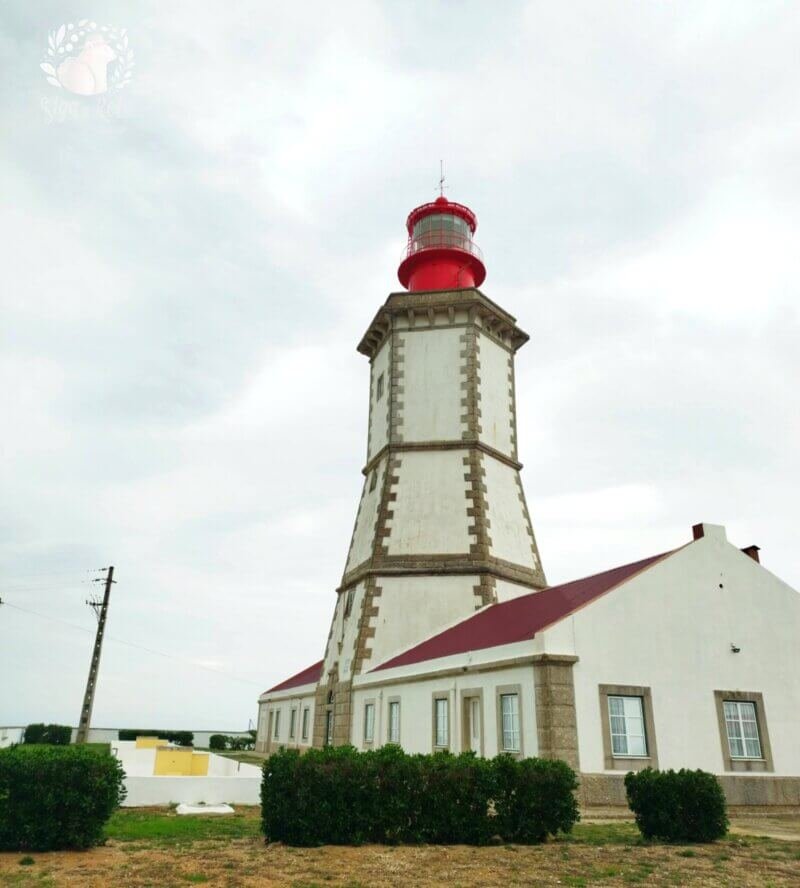 O Farol do Cabo Espichel iluminado pelo sol poente, cercado pela paisagem natural.