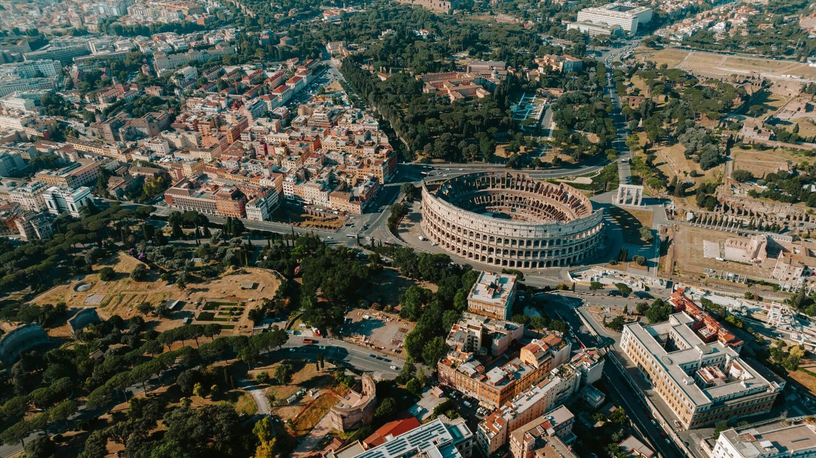 Imagem aérea do Coliseu de Roma, destacando sua grandiosidade e os arredores históricos da cidade.
